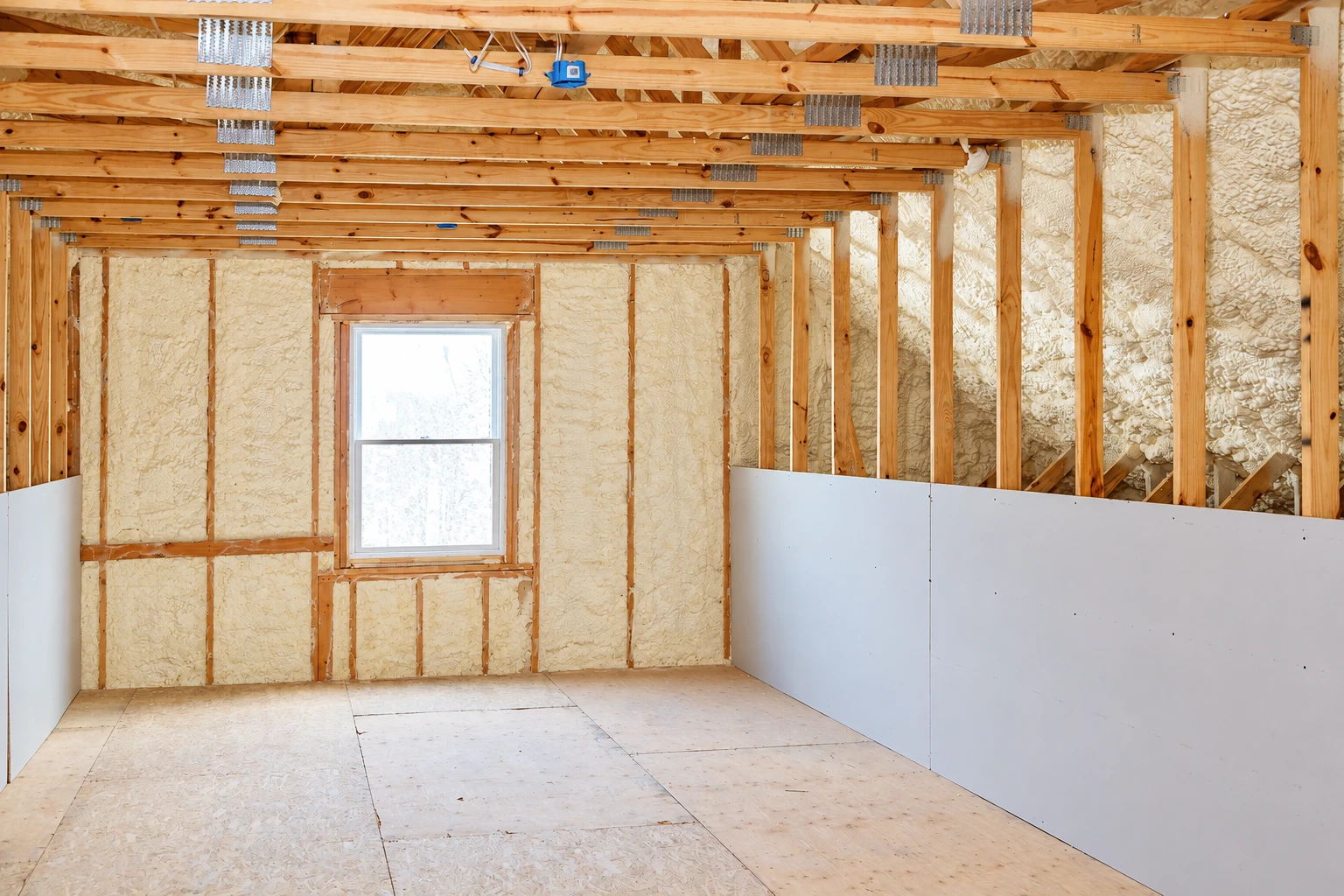 Unfinished attic room with pale foam insulation between exposed wooden framing and a window.