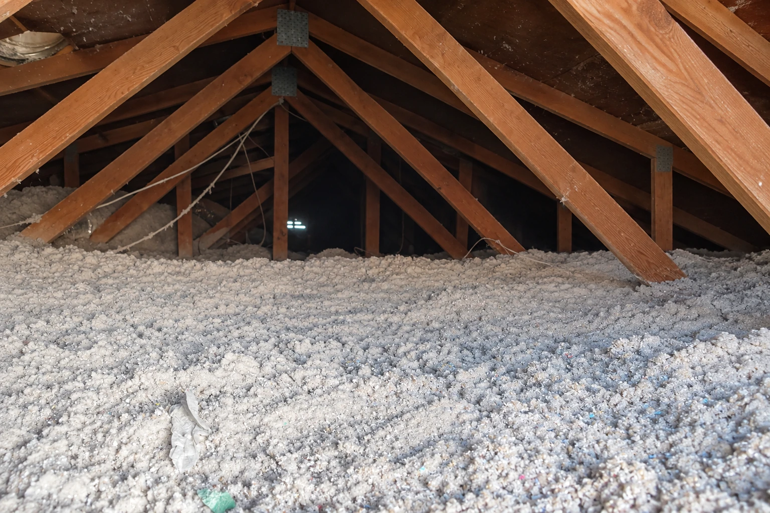 Loose-fill insulation covers an attic floor beneath exposed wooden roof trusses.