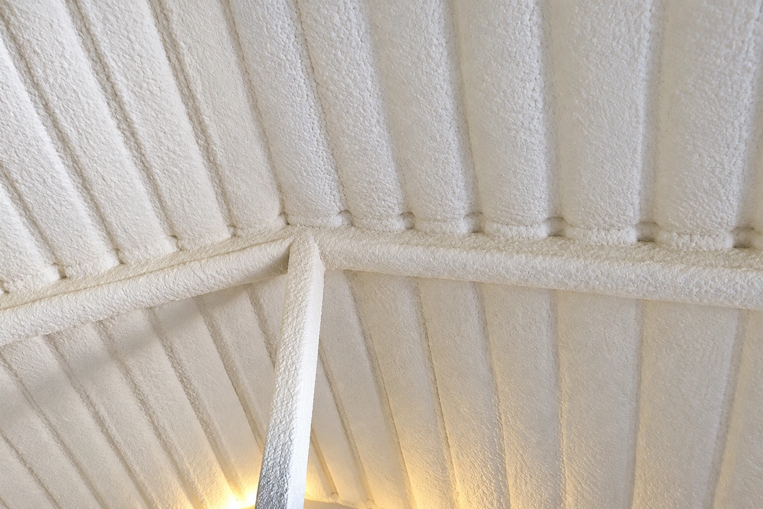 White spray foam coats the underside of a roof and its supporting beams.