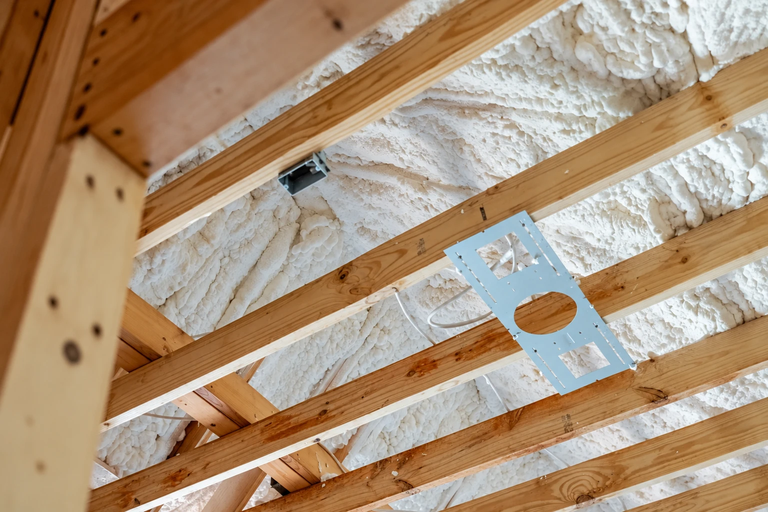 White open-cell spray foam covers the underside of a wooden roof framed with rafters.