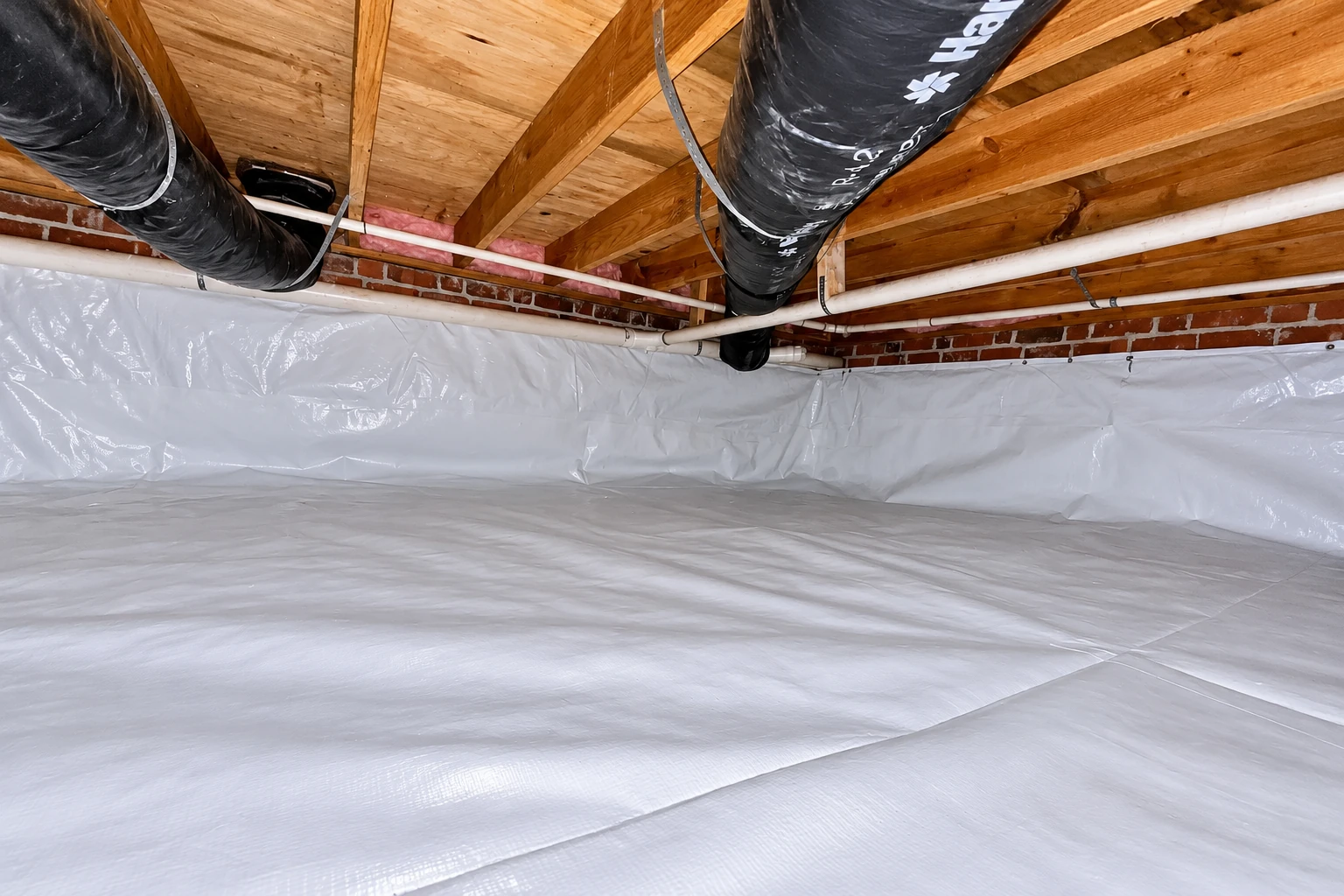 A crawl space floor and lower brick walls are covered with a white vapor barrier beneath exposed joists, ducts, and pipes.